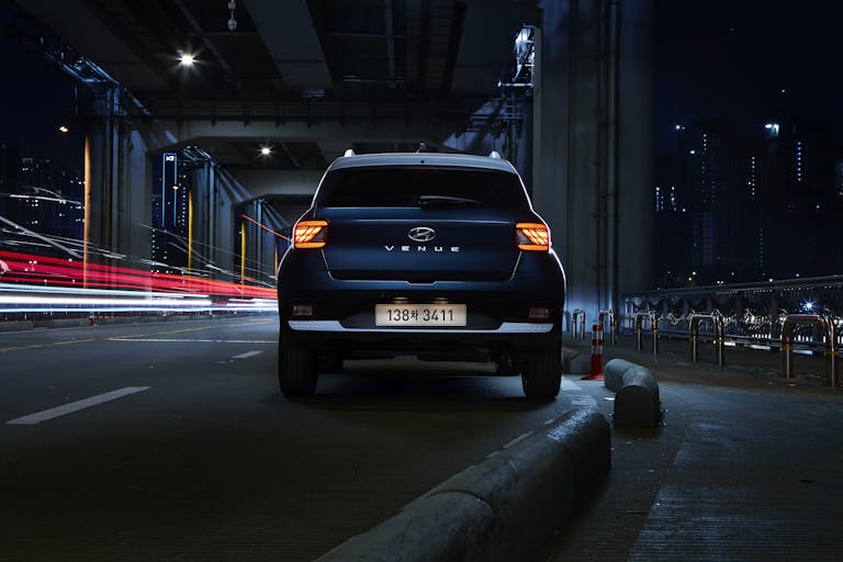 A Hyundai Venue SUV under a city bridge in Seoul at night with striking light trails.