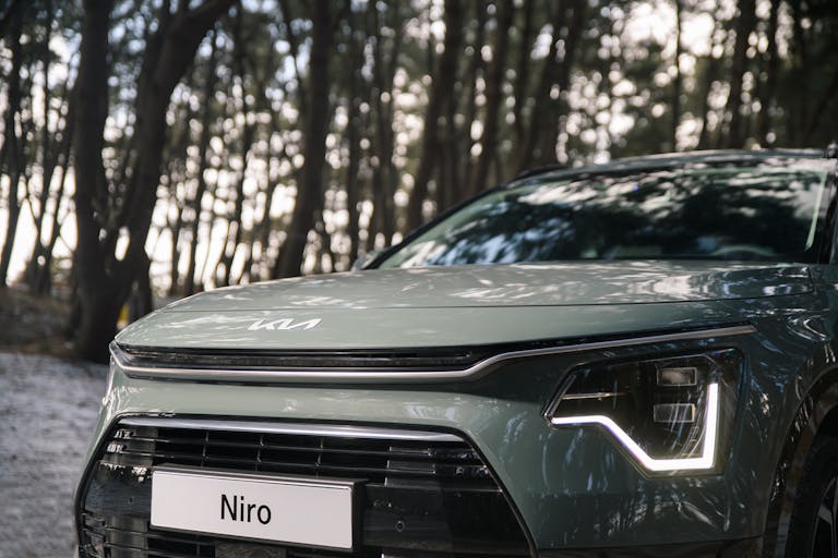 Close-up of a modern car's front featuring sleek headlights in a forest setting.
